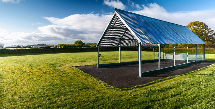 Outdoor Classroom Open structure canopy on green grass with clear blue sky and distant trees.