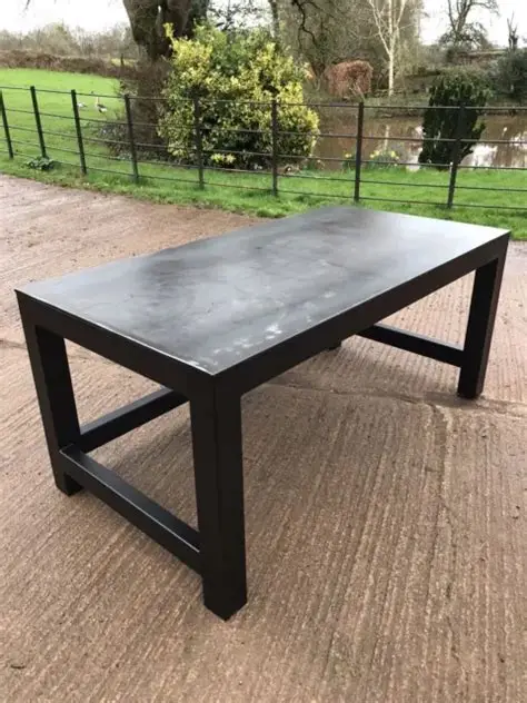 Custom Steel Table A sturdy black wooden table on a gravel surface, with a green landscape in the background.