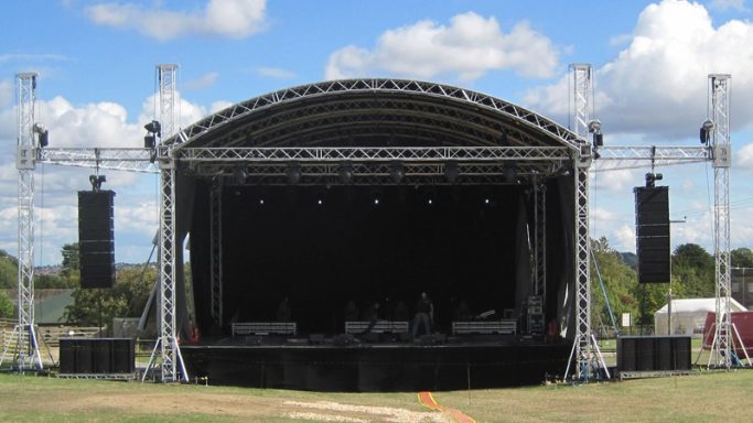 Outdoor Stage Shelter Outdoor concert stage with a large canopy and sound equipment, set up in a grassy area.