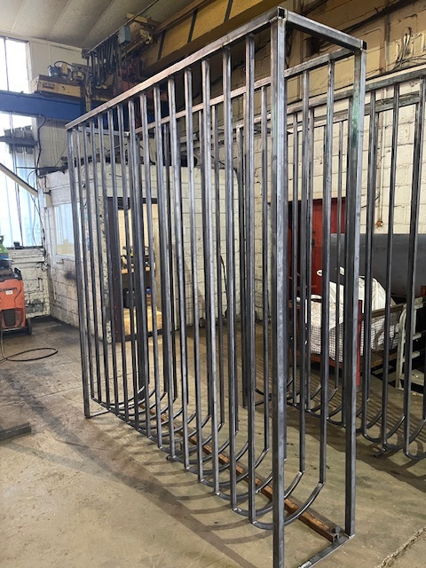Custom Racking A large metal frame with vertical bars, situated in a workshop.